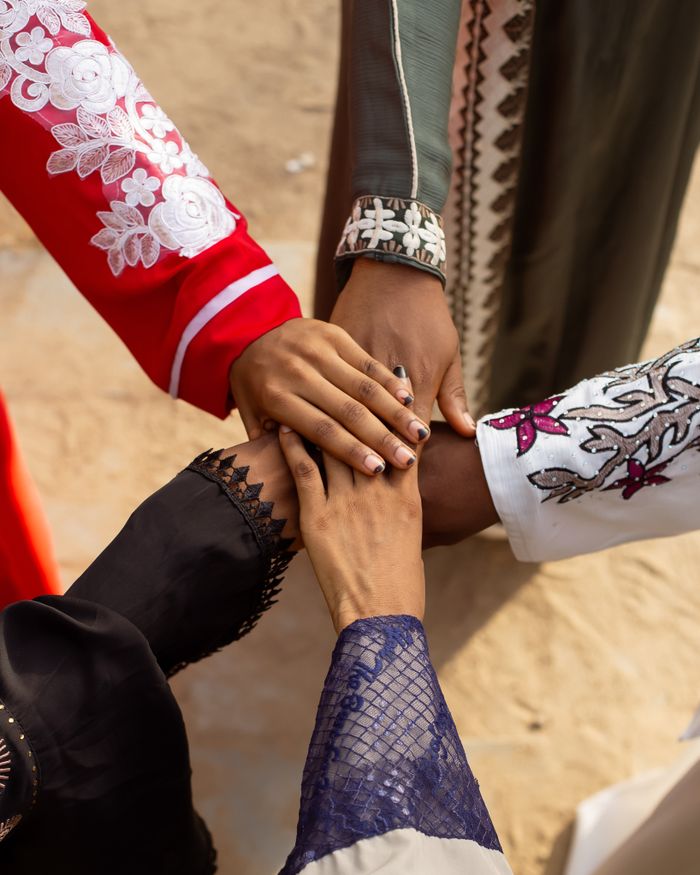Services A group of people joining hands wearing colorful traditional attire outdoors, symbolizing unity.